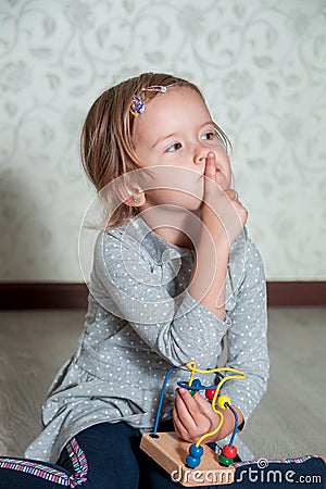 Child playing with maze. Little girl thinking a finger near the mouth. Educational toy. Stock Photo