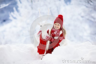 Child playing with reindeer in snow on Christmas vacation. Winter outdoor fun. Kids play in snowy park on Xmas eve. Little girl in Stock Photo