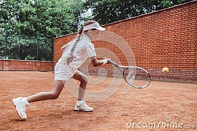 Child playing tennis on outdoor clay court. Full length shot of a tanned little girl on tennis court. Girl child playing tennis Stock Photo