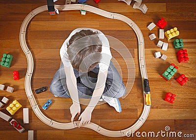 Child playing with toys train and railroad while sitting on the wooden floor in his room. Top view Stock Photo