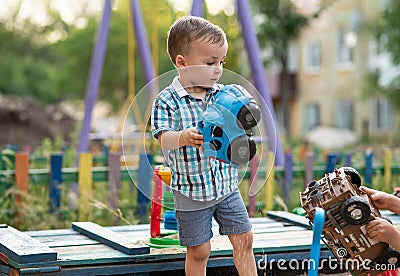 A child plays in the playground with toys in the sandbox. A toddler boy plays in the sand with a car on a summer day Stock Photo