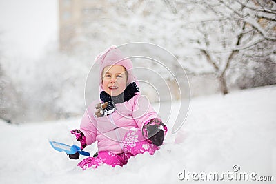 The child plays with snow in the winter. A little girl in a bright jacket and knitted hat, catches snowflakes in a winter park for Stock Photo