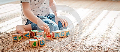 child plays with wooden blocks with letters on the floor in the room a little girl is building a tower at home or in the Stock Photo