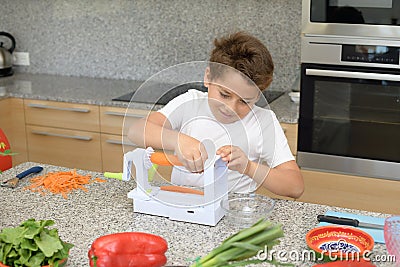 Child preparing lunch. Putting carrots in a manual machine Stock Photo