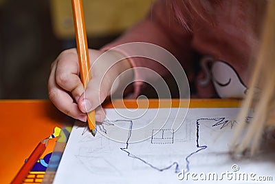 Child preschooler learns to draw and write in notebooks at home in the evening under the light from a desk lamp. Stock Photo