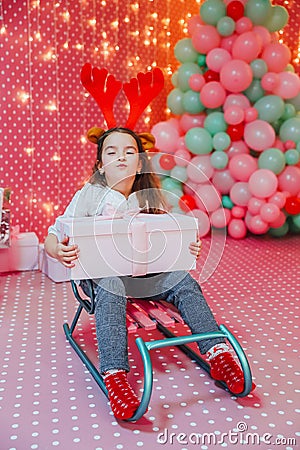 Child, present and sledge on the pink celebration background. Greedy child is frowning, keeping box close to her chest. Stock Photo