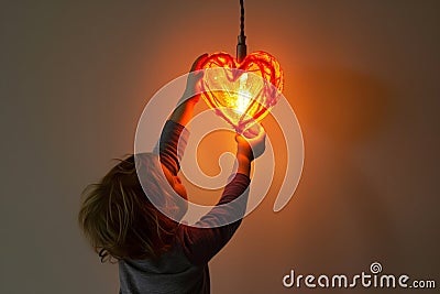 child reaching for a heartshaped pendant lamp Stock Photo