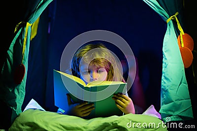 Child reading a book in the dark home. Kids bedtime. Boy read book in bed. Stock Photo