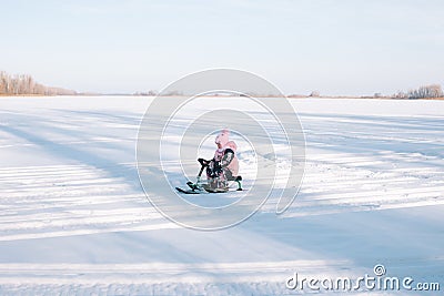 Child rides snowcat on snowy road. Little girl in pink warm jacket enjoys walk in nature and sledding on frozen river on Stock Photo