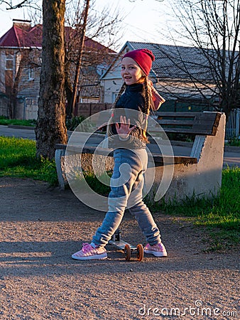 Child riding on kickscooter alone. Blonde cute girl on scooter on spring city park street background. Active lifestyle Stock Photo