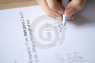 child, right-handed schoolchild hesitantly solves difficult task of adding numbers, 5th grade student writes down numbers in Stock Photo