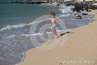 Child running through water close to shore along the sea beach. A boy runs along the sea coast. Rest of children on Stock Photo