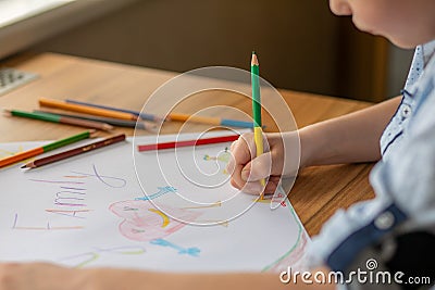 The child`s hand holds a pencil and draws a picture. The inscription on the drawing is Family. On the table lie pencils in bulk Stock Photo