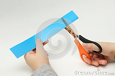 Child`s hands scissor a strip of blue paper on white background Stock Photo