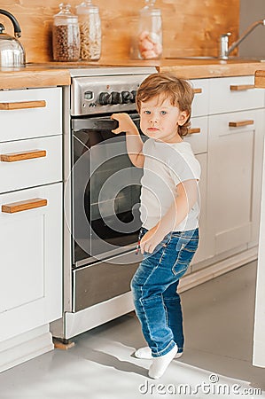 Child safety at home concept. Little baby reaching for hot pan on stove in kitchen, empty space Stock Photo