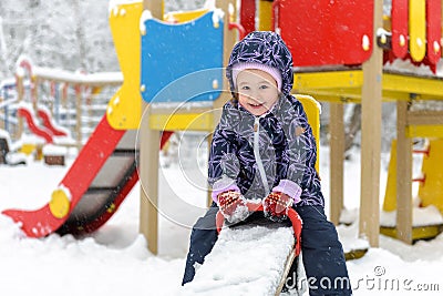 Child on seesaw in winter, little kid having fun on snowy playground Stock Photo