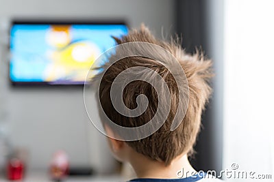 A child of several years standing back in the room looking at the television. Stock Photo