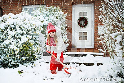 Child shoveling snow. Little girl with spade clearing driveway after winter snowstorm. Kids clear path to house door after Stock Photo