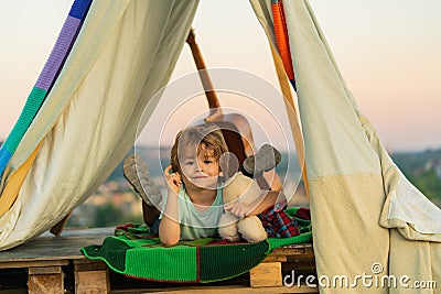 Child sitting in tent at summer camp. Camp dream. Kid dreams in tent outdoor. Childhood dream. Daydreamer child. Dreams Stock Photo