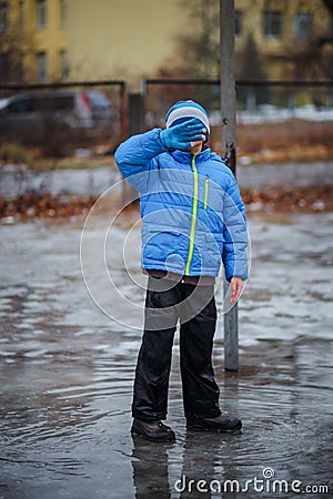 A child in snowboots boots is standing in a puddle of melted snow. Ice on the roads in the city. Not cleaned from snow and ice Stock Photo