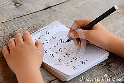 Child solves math examples. Child holds a marker in his hand and writes answers to multiplication examples in a notebook Stock Photo