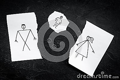 Child suffers from a divorce. Torn sheet of paper with drawn man, woman and child, wedding rings between parts on black Stock Photo