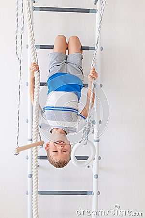 A child on the Swedish wall plays sports at home, a boy climbs a ladder with a rope, the concept of sports and health Stock Photo