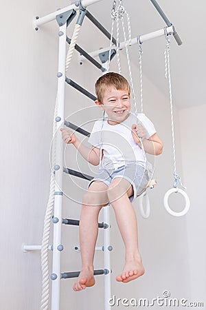 A child swings on a swing on the Swedish wall and does sports at home, the concept of sports and health Stock Photo
