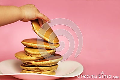 A child takes a pancake from a stack, pink background Stock Photo