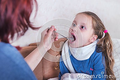 Child taking medicine. Sick girl with scarf lying on bed Stock Photo