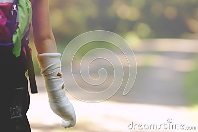 A child or teenage kid with its forearm in plaster cast goes hiking happily on a forest path lying in bright sun light. Stock Photo