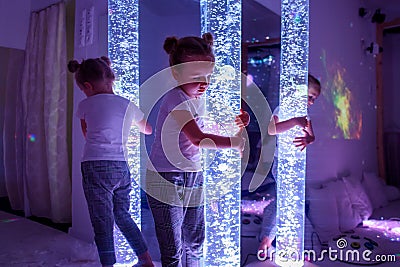 Child in therapy sensory stimulating room, snoezelen. Autistic child interacting with colored bubble tube lamp during therapy. Stock Photo