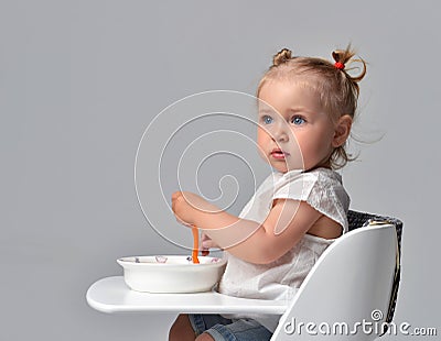 child toddler kid sitting with plate and spoon on white baby chair table Stock Photo