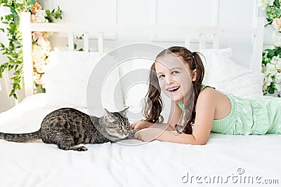 A child is torturing an animal, a little girl with a cat is lying on the bed, the concept of a child`s friendship with animals Stock Photo