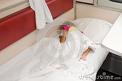 A child in train sleeping wrapped in a sheet in the lower place in the second-class compartment wagon Stock Photo