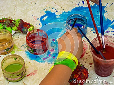 Child using paint brush and with paint supplies and making a mess.. Stock Photo