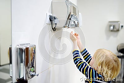 Child using restroom. Little boy dries his hands in the toilet with an automatic dryer. Taking care of the hygiene of children in Stock Photo