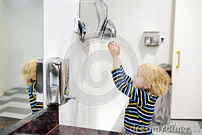 Child using restroom. Little boy dries his hands in the toilet with an automatic dryer. Taking care of the hygiene of children in Stock Photo