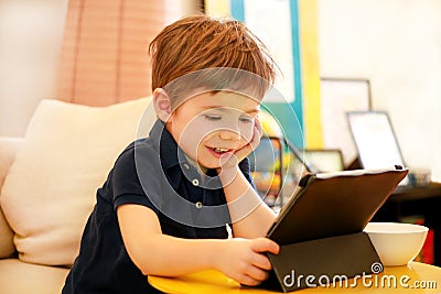 Child using tablet pc on bed at home. Cute boy on sofa is watching cartoon, playing games and learning from laptop. Education, fun Stock Photo