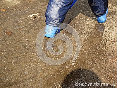 The child walks through puddles in rubber boots in the spring Stock Photo