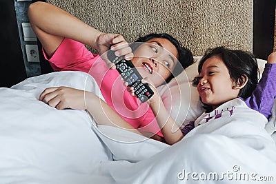 Asian Little Boy On Bed Wants to Take Over Television Remote Control from His Mother. Family Feud Stock Photo