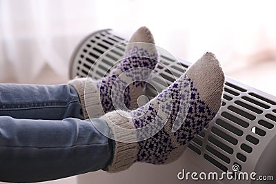 Child warming feet on electric heater at home, closeup Stock Photo