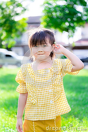 Child was holding cute little white grass flower on his ears. Sweet smile girl looking at camera. Evening sun in summer. Stock Photo