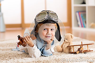 Child weared pilot or aviator plays with a toy airplane at home in nursery room. Concept of dreams and travels. Stock Photo