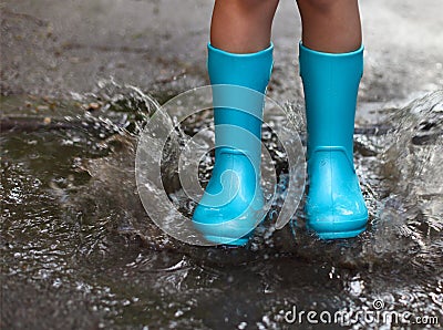 Child wearing blue rain boots jumping into a puddle Stock Photo