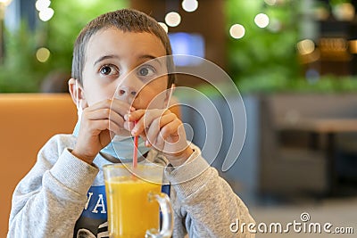 A child wearing a mask in a cafe during a pandemic. A boy in a cafe drinks sea buckthorn tea in a cafe during a pandemic Stock Photo