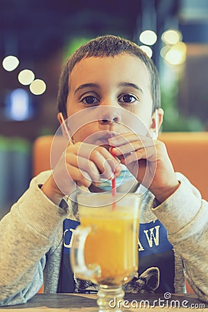 A child wearing a mask in a cafe during a pandemic. A boy in a cafe drinks sea buckthorn tea in a cafe during a pandemic. tioned Stock Photo