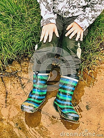 Child wearing rain boots , sits at muddy puddle Stock Photo