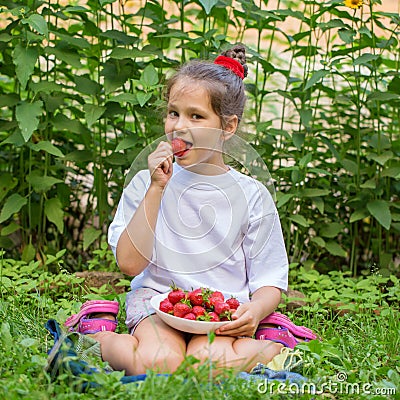 Child in white T-shirt eating strawberries Stock Photo