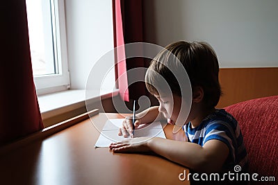 The child writes down the answer to the solution of the example in a copybook. A mathematics task. A boy diligently learns to Stock Photo